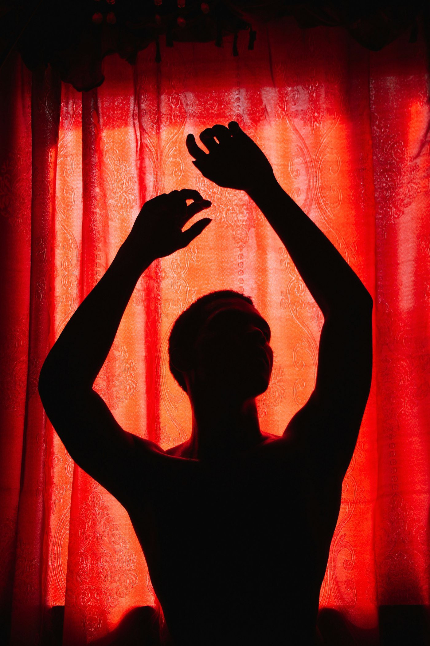 Silhouette d'un danseur, bras levés, devant un rideau rouge