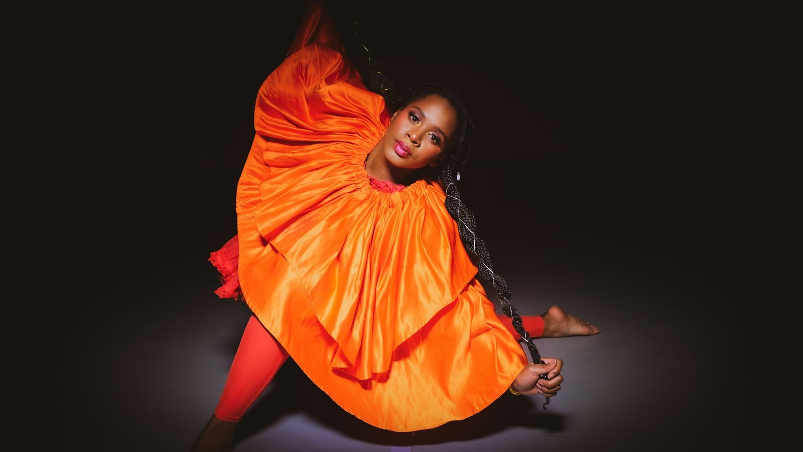 Danseuse en costume orange, le corps arqué, sur un plateau plongé dans le noir